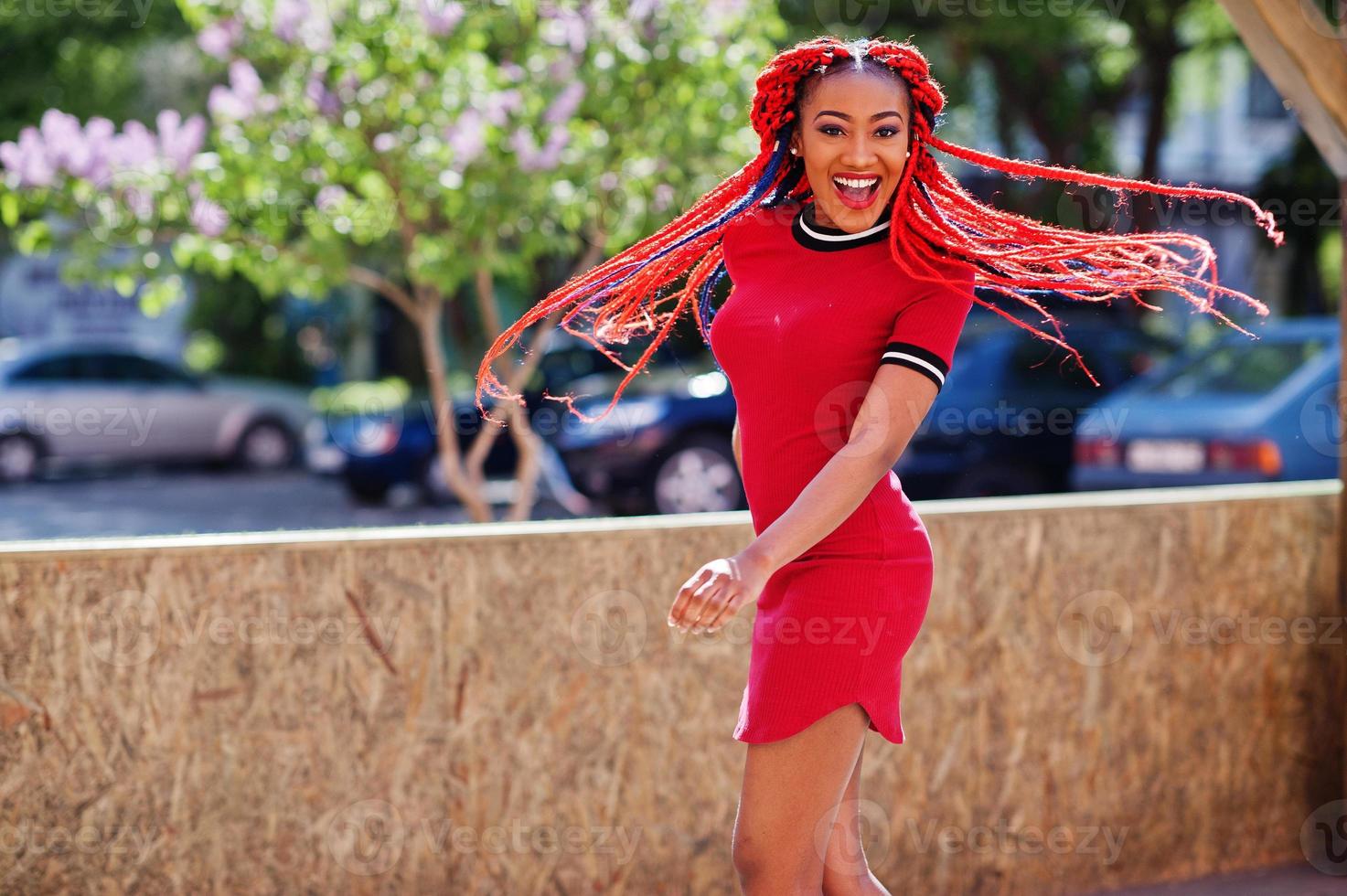 Cute and slim african american girl in red dress with dreadlocks in motion having fun on street. Stylish black model. photo