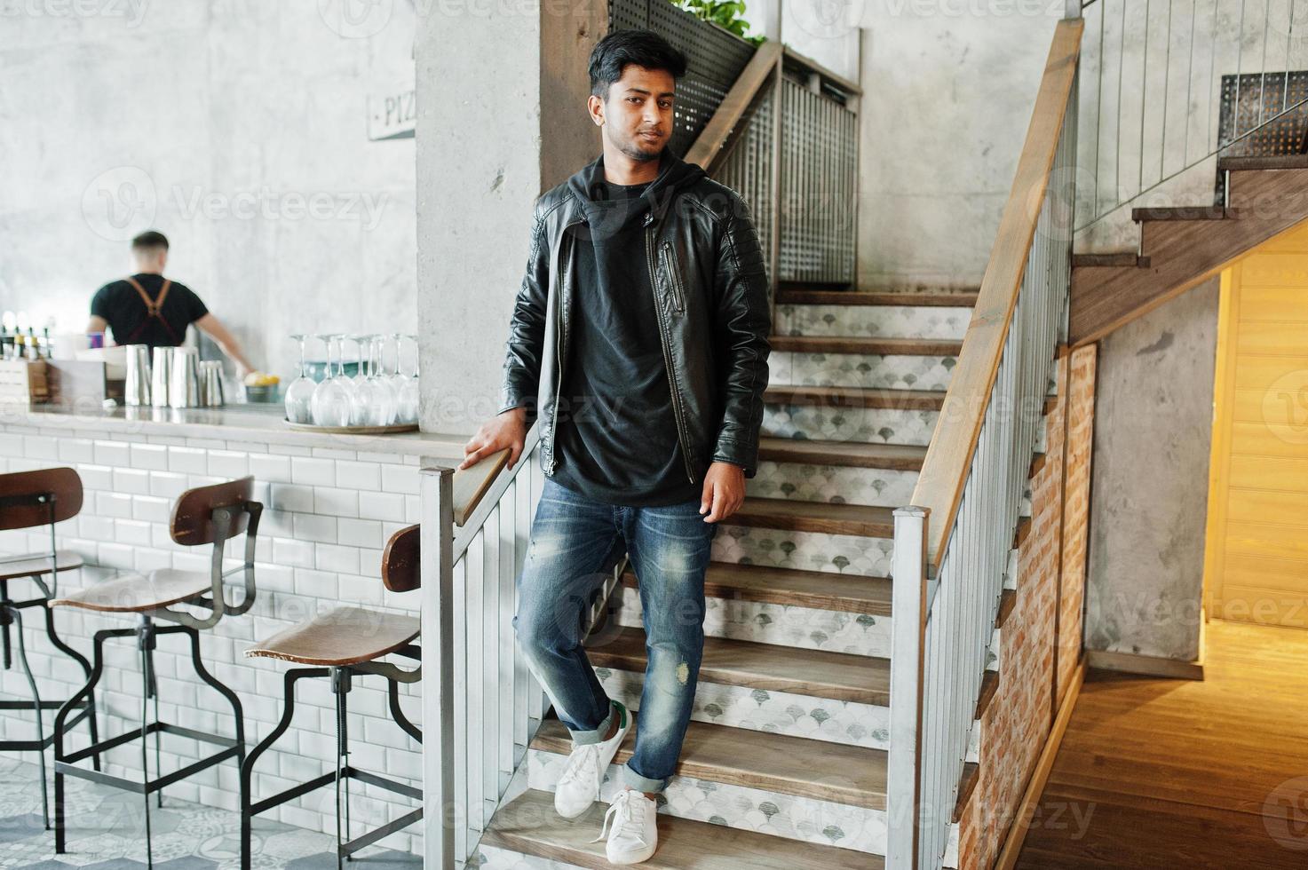 un joven asiático casual y elegante vestido con una chaqueta de cuero parado en las escaleras del café. foto