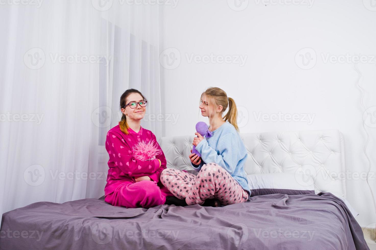 Two friends girls in pajamas having fun on bed at room. photo