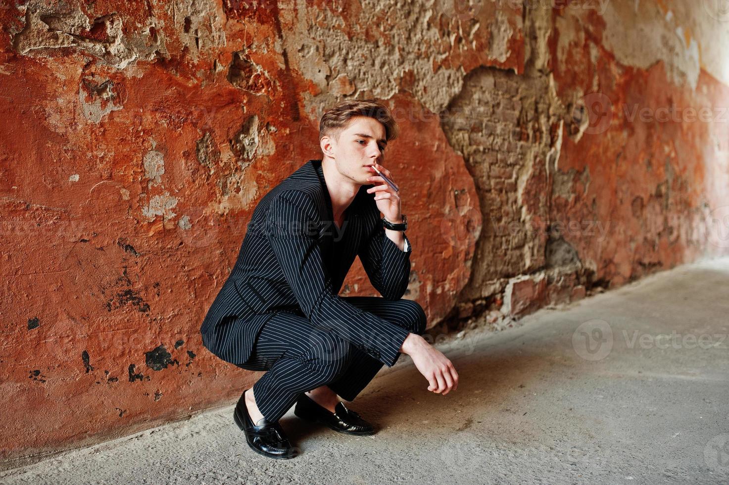 Young macho boy wear on blac stylish jacket smoking cigarette on streets. photo