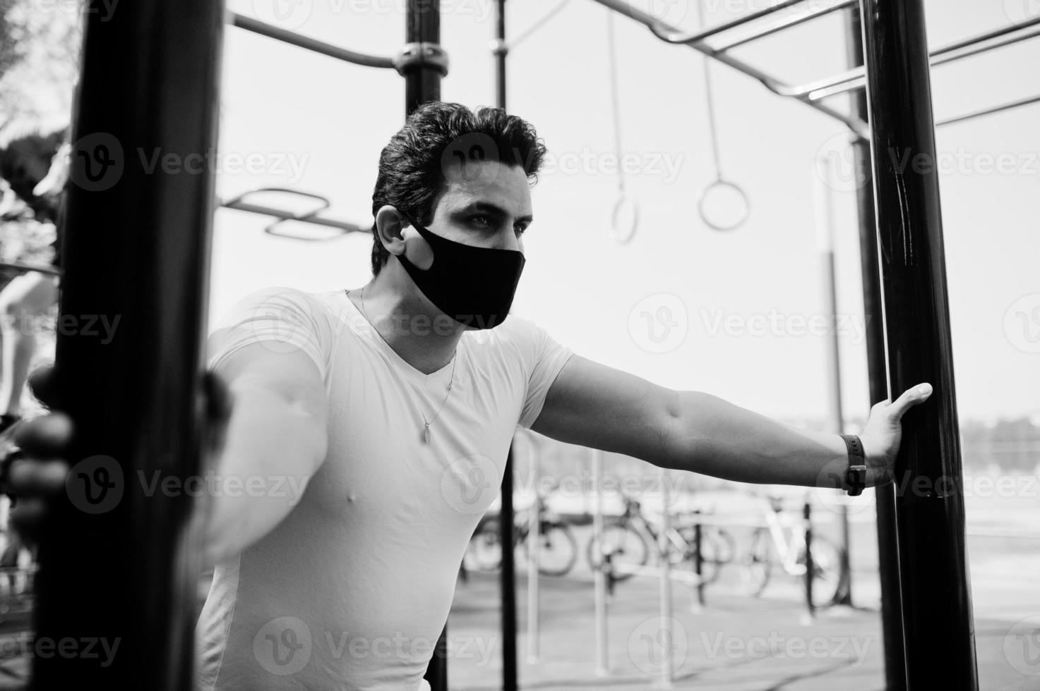 Portrait sports arabian man in black medical face mask doing workout exercises in outdoor gym place during coronavirus quarantine. photo