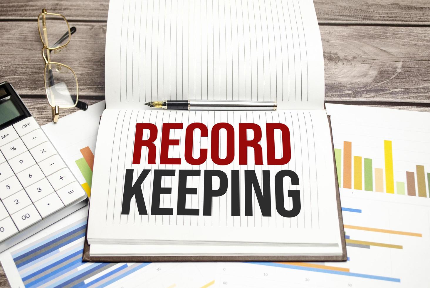 RECORD KEEPING words on brown diary and glasses, calculator and pen on wooden desk photo