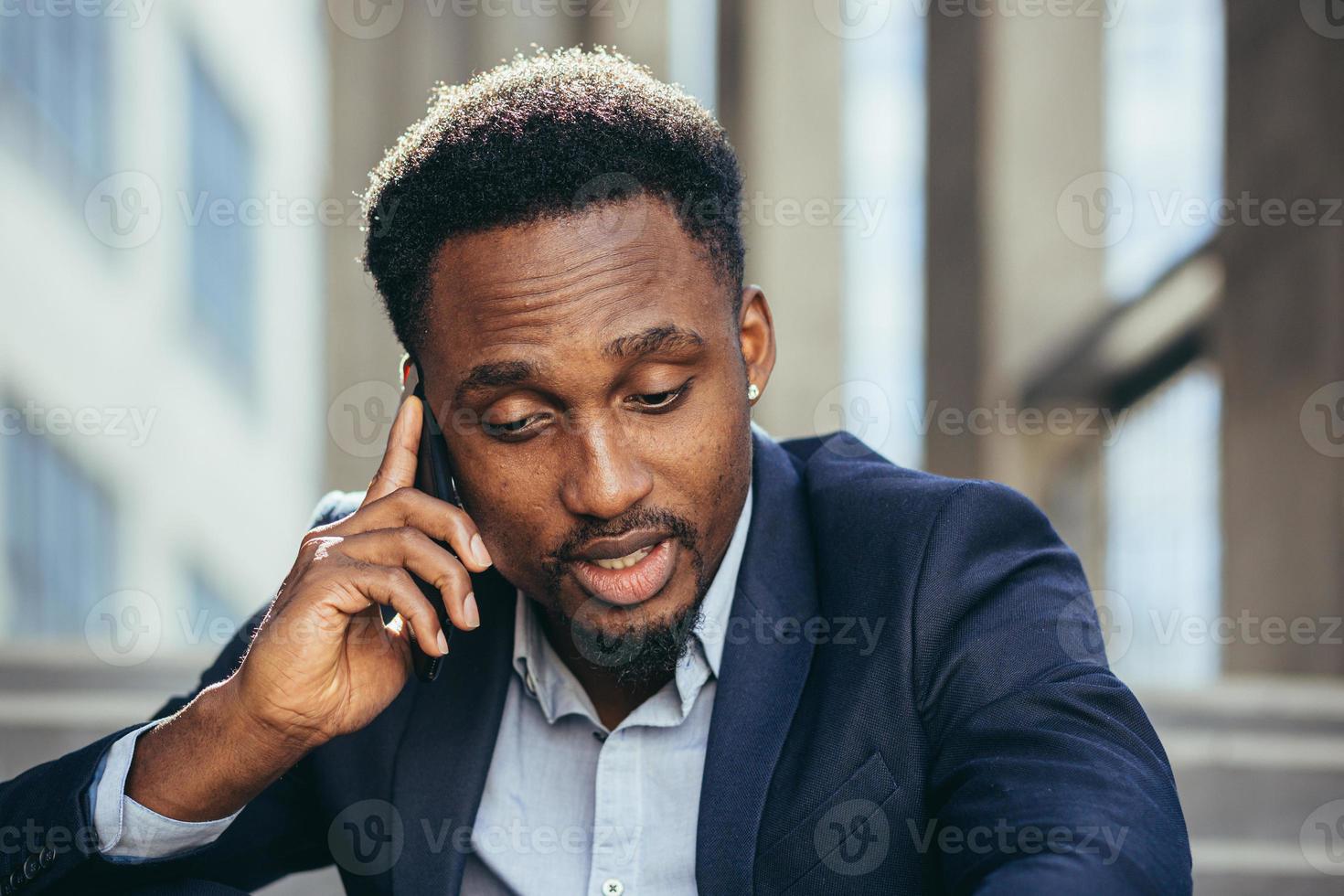 Depressed african american businessman telling sad news talking on cell phone sitting photo