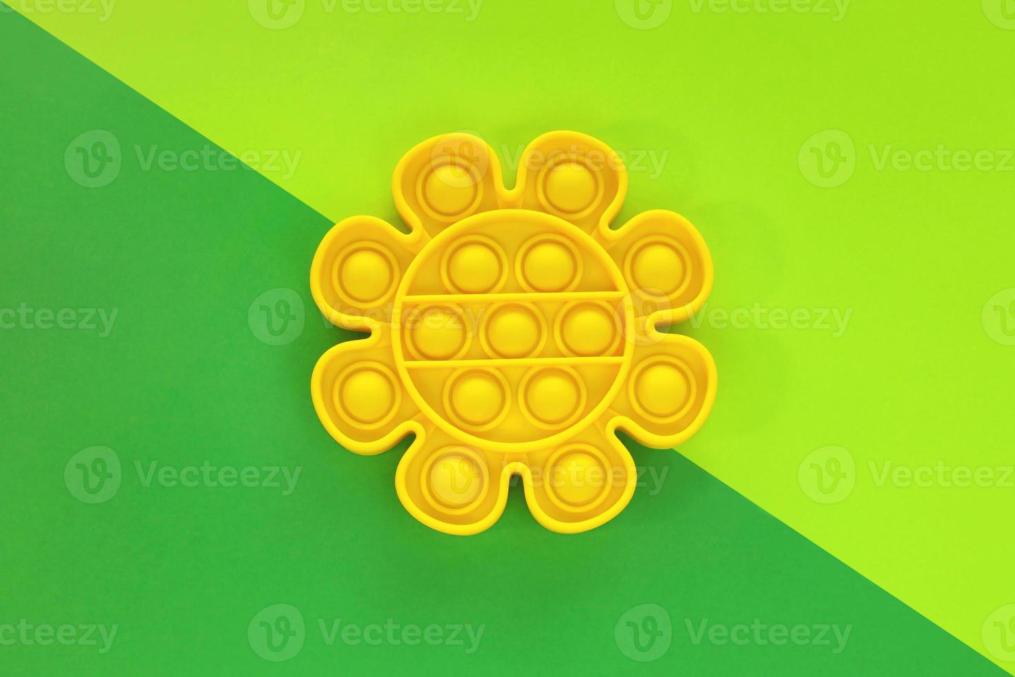 Yellow flower pop it toy. New trendy anti stress sensory silicone bubble fidget toy on summer dark green and light green color paper diagonal background. Education for kids, relaxation for adults. photo