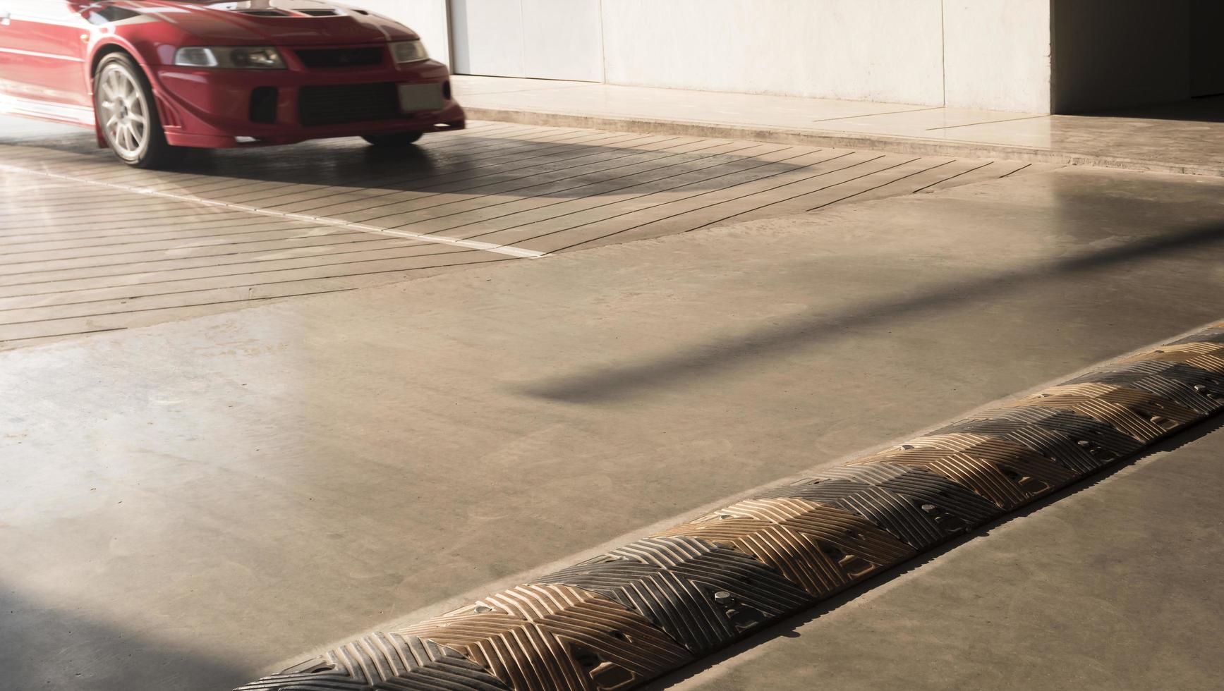 Samutsakhon, Thailand, 2020 - Sunlight on surface of speed bumper on cement floor with blurred motion of red car is running on entrance way into parking garage photo