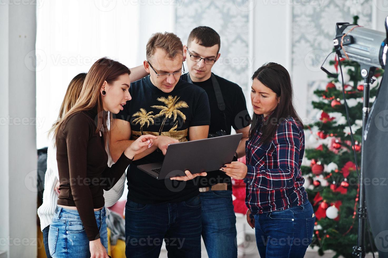 Photographer explaining about the shot to his team in the studio and looking on laptop. Talking to his assistants holding a camera during a photo shoot. Teamwork and brainstorm.