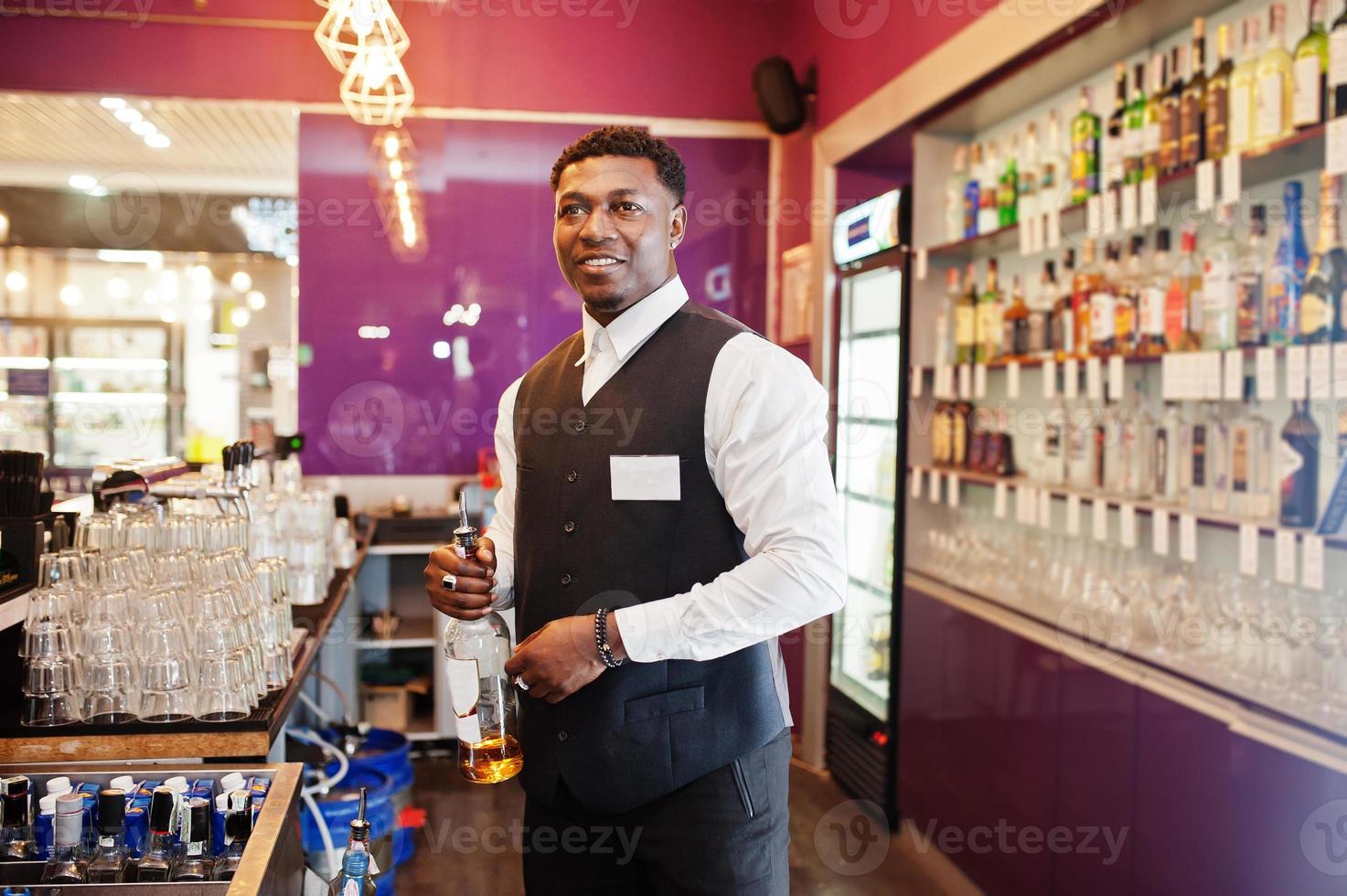 African american bartender at bar holding bootle. Alcoholic beverage preparation. photo