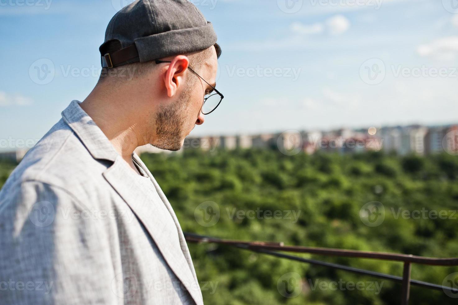 Dreamer stylish macho man in gray suit, hat and glasses posed on the roof. photo