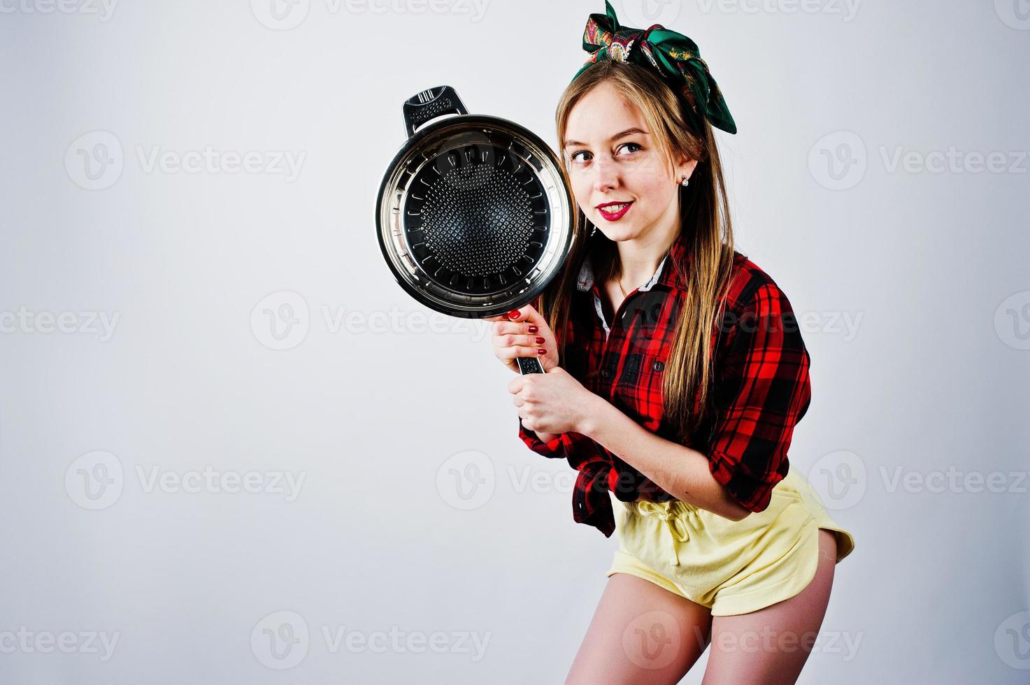 joven ama de casa divertida en camisa a cuadros y pantalones cortos amarillos pin up estilo con sartén aislado sobre fondo blanco. foto