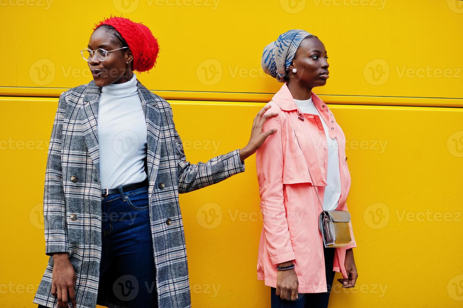 Two young modern fashionable, attractive, tall and slim african muslim womans in hijab or turban head scarf and coat posed against yellow bus. photo
