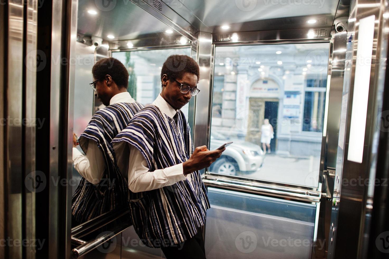 hombre africano con ropa tradicional y gafas con teléfono móvil en elavator o ascensor moderno. foto