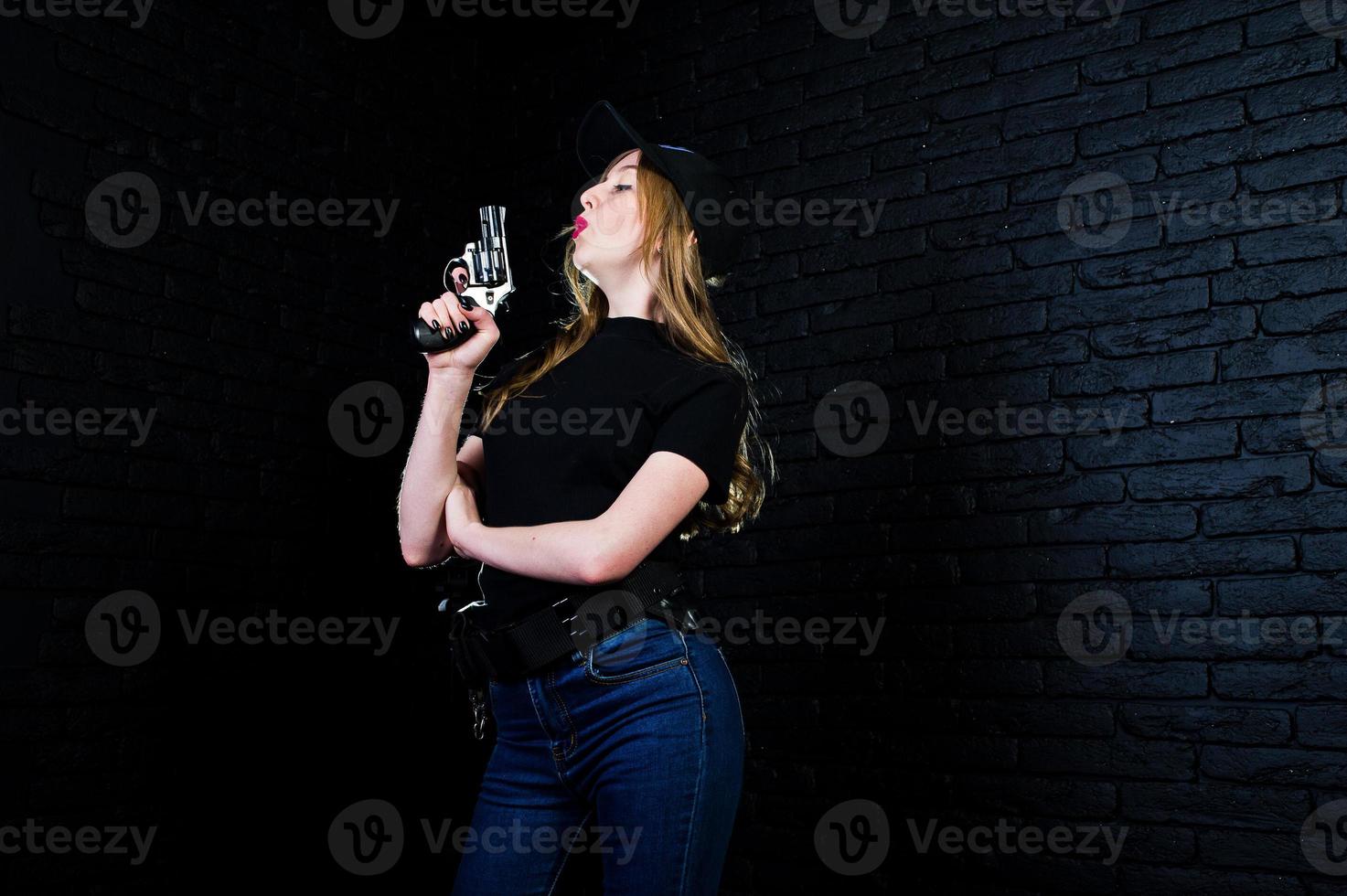 FBI female agent in cap and with gun at studio against dark brick wall. photo