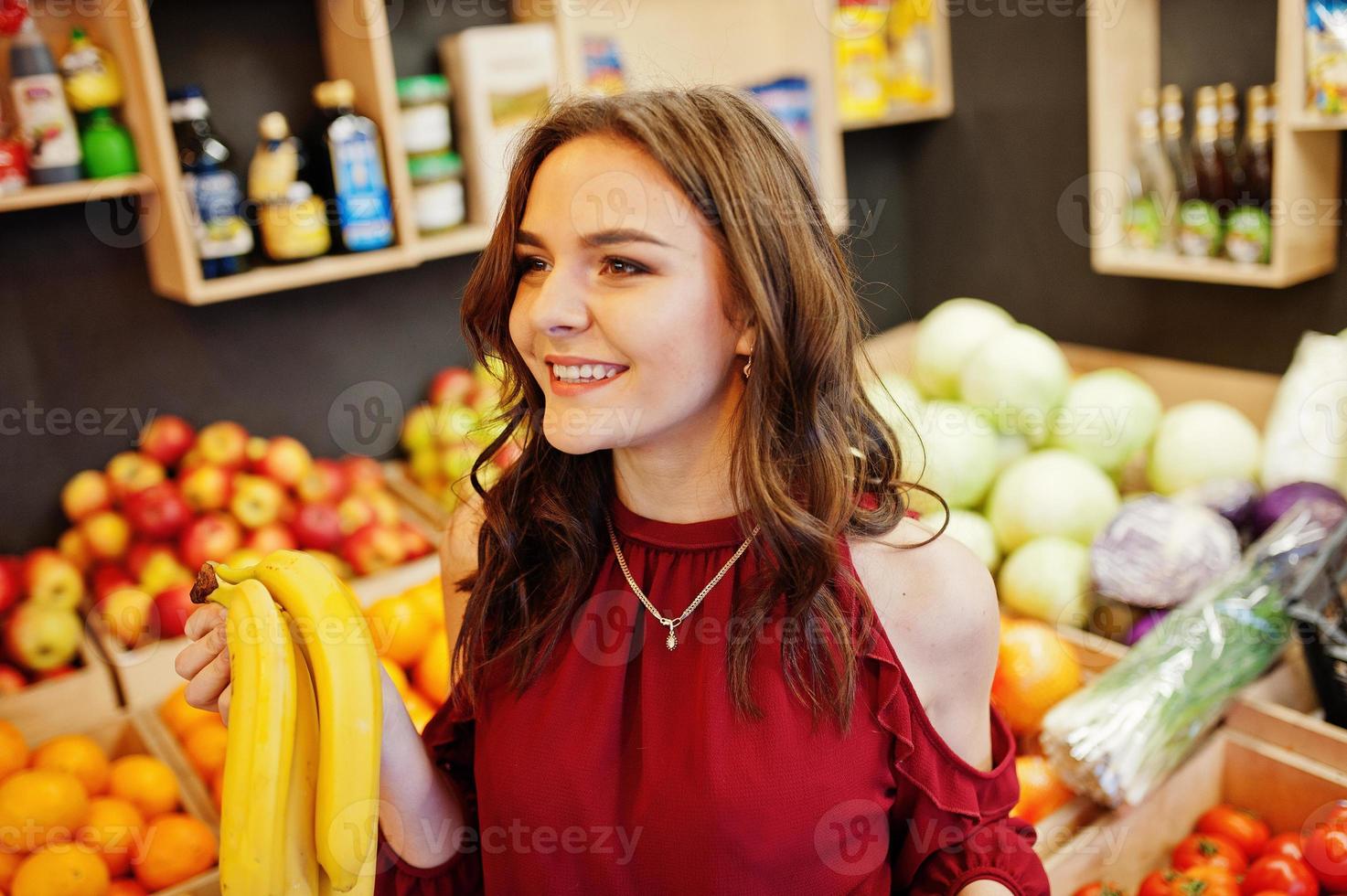 Girl in red holding bananas on fruits store. photo