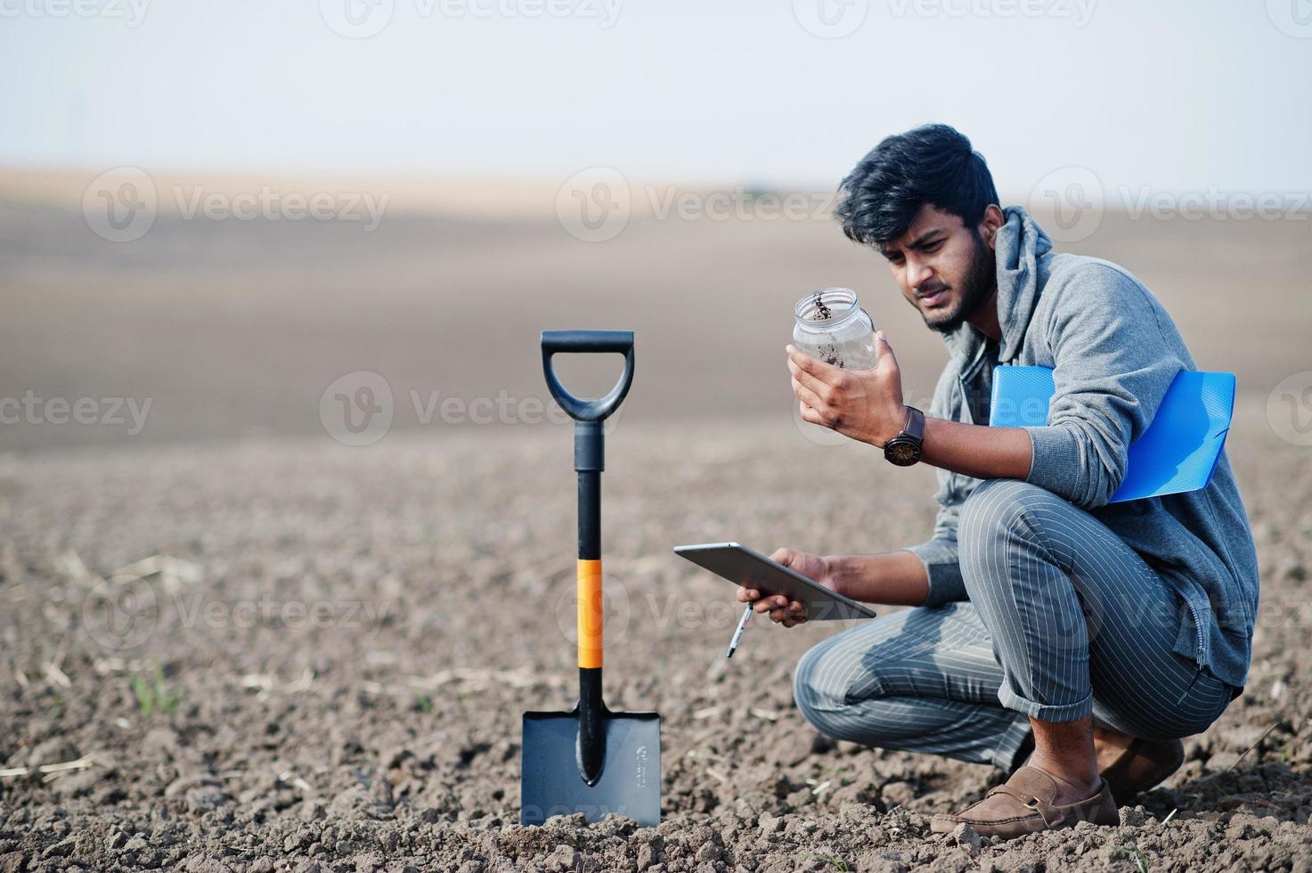 South asian agronomist farmer with shovel inspecting black soil. Agriculture production concept. photo