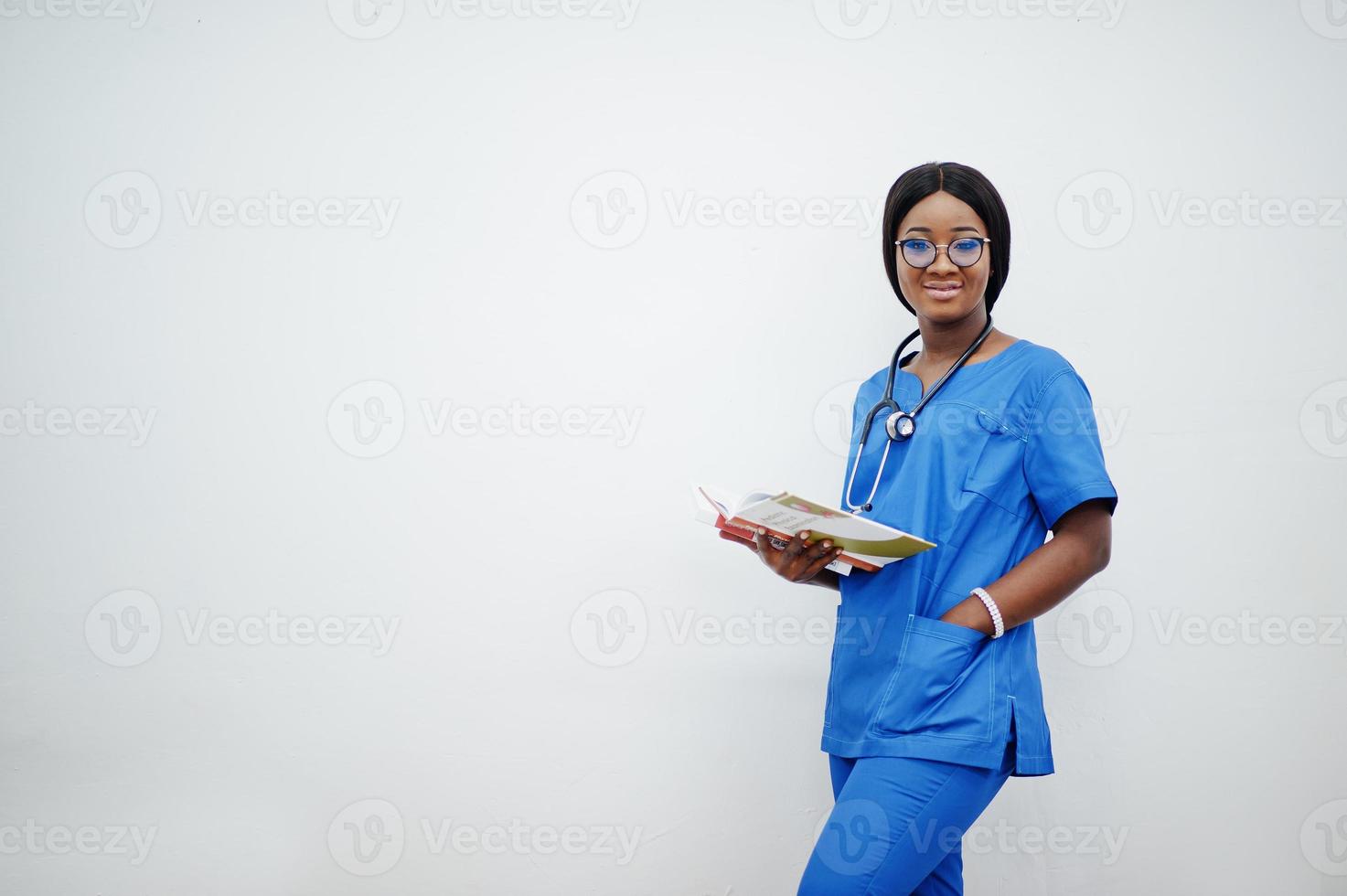 Portrait of happy female african american young doctor pediatrician in blue uniform coat and stethoscope with books at hands isolated on white. photo