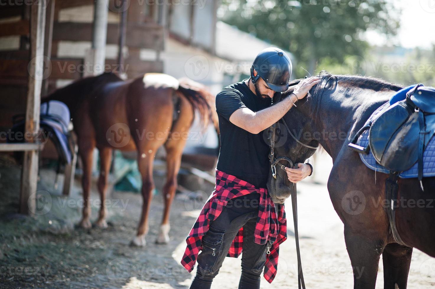 Arab tall beard man wear in black helmet with arabian horse. photo
