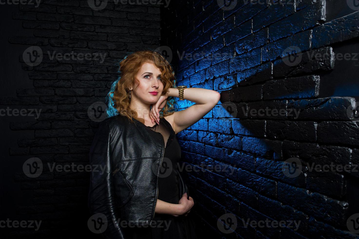 Curly hair girl at leather jacket on studio against black brick wall. photo