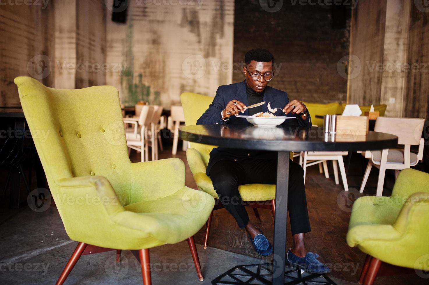 Fashionable african american man in suit and glasses sitting at cafe and eating salad. photo