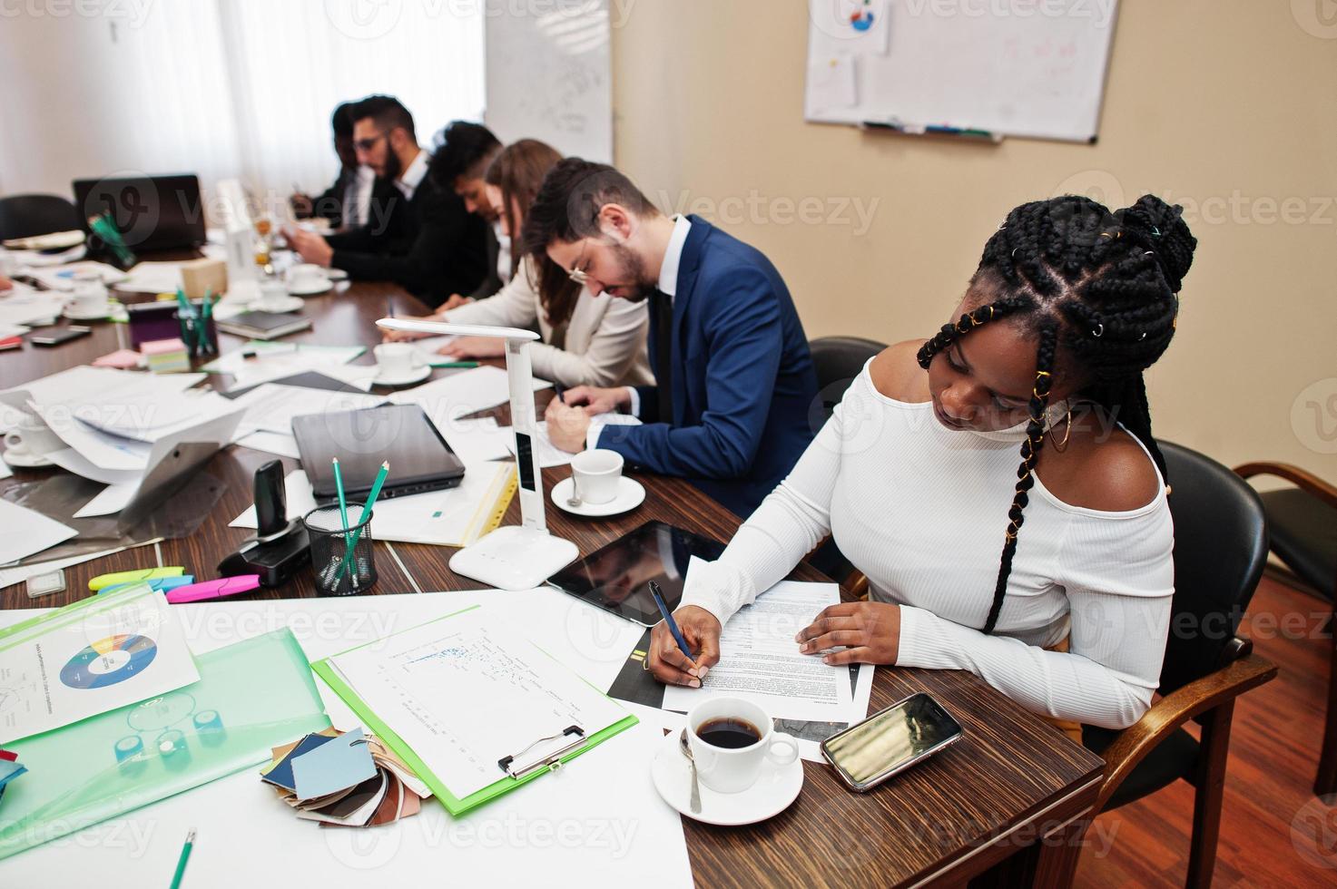 Multiracial business team addressing meeting around boardroom table, working together and write something on papers. photo