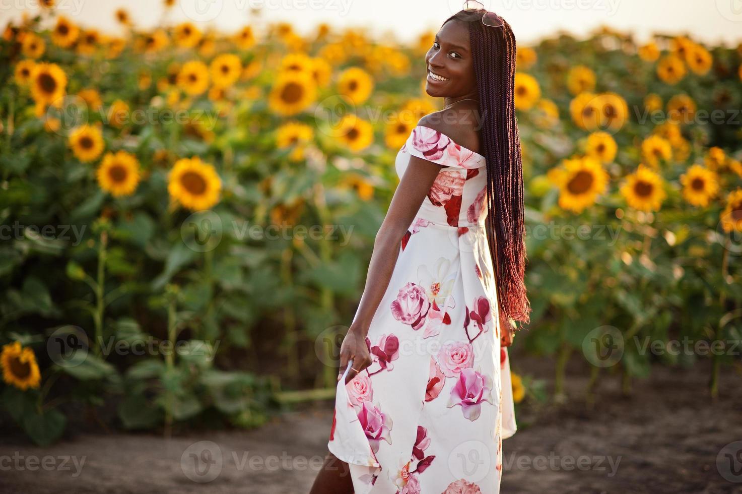 una mujer negra muy joven usa una pose de vestido de verano en un campo de girasoles. foto