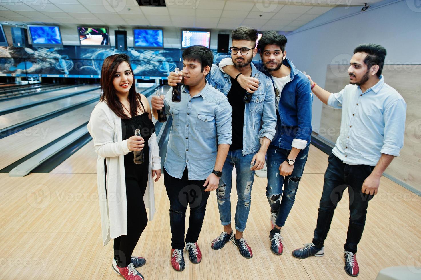 Group of five south asian peoples having rest and fun at bowling club. Holding cold soda drinks from glass bottles. photo