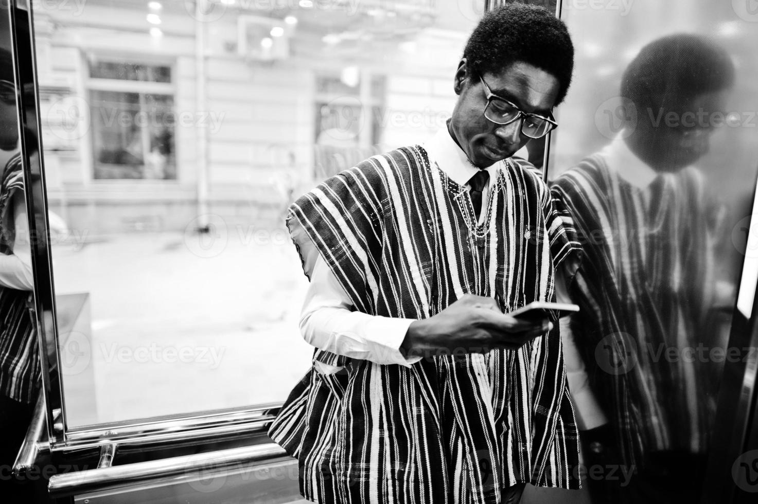 hombre africano con ropa tradicional y gafas con teléfono móvil en elavator o ascensor moderno. foto