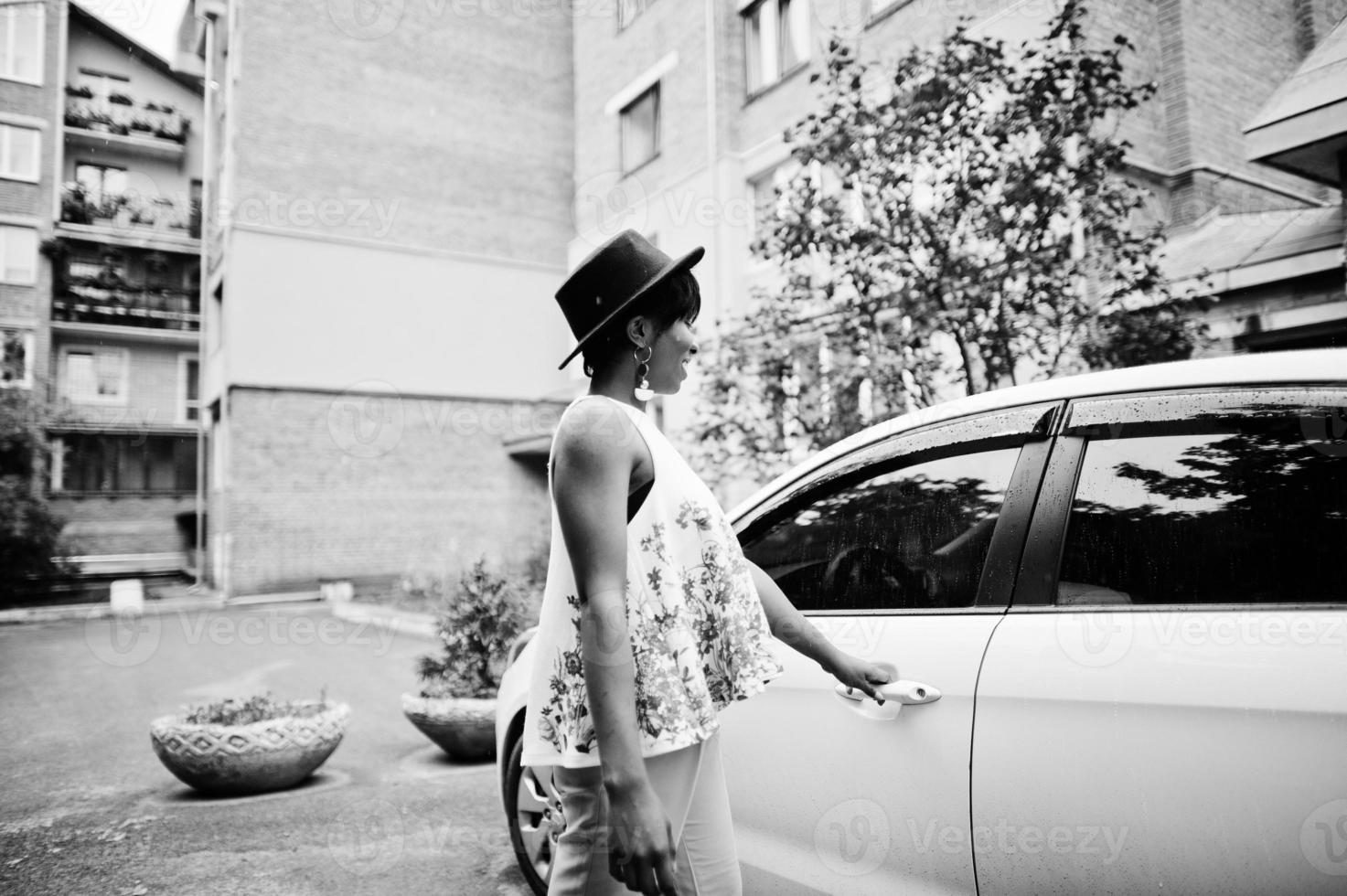 Amazing african american model woman in green pants and black hat posed near white door of car. photo
