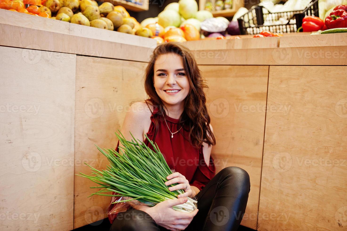 chica de rojo con cebollas verdes en la tienda de frutas. foto