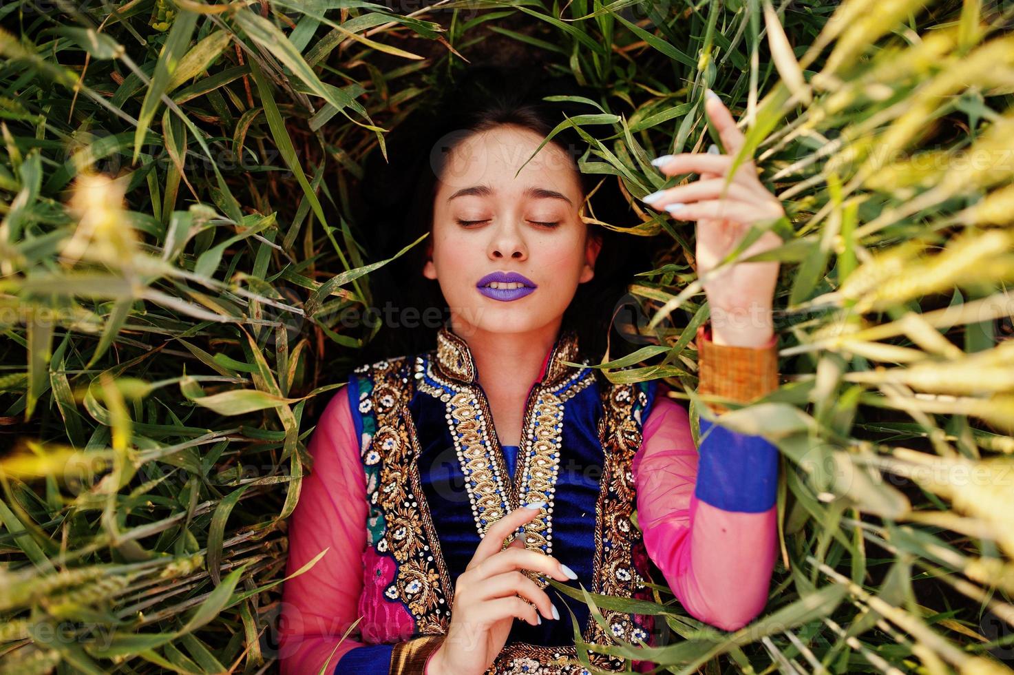 tierna niña india en sari, con maquillaje de labios violetas posada en el campo al atardecer. modelo indio de moda. foto