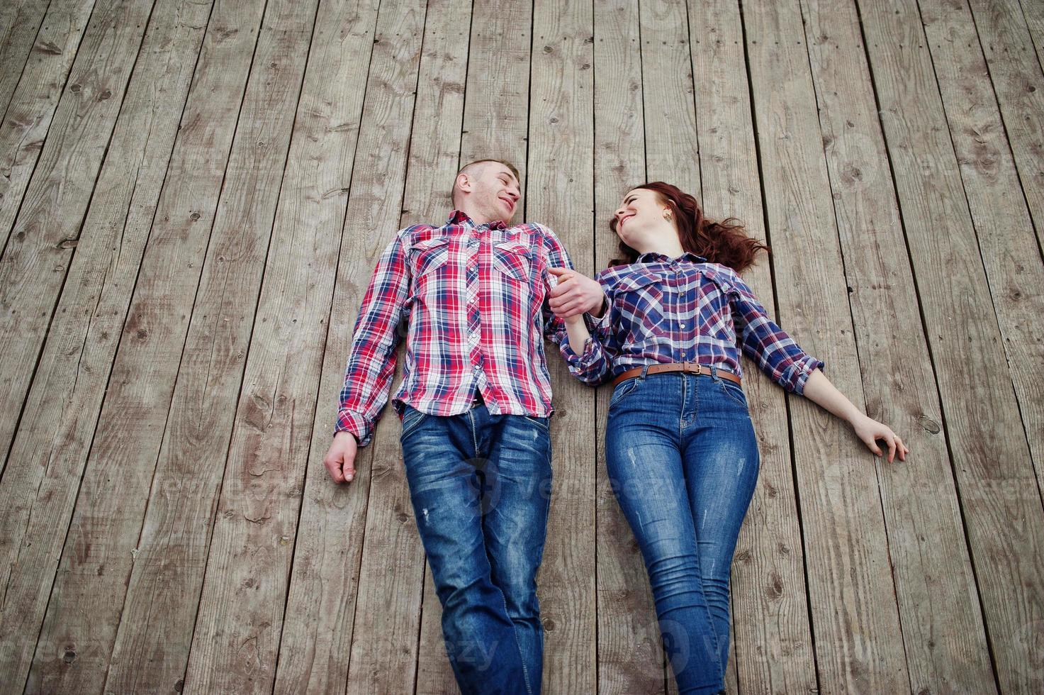 una pareja elegante se viste con una camisa a cuadros enamorada y se acuesta en las tablas. foto