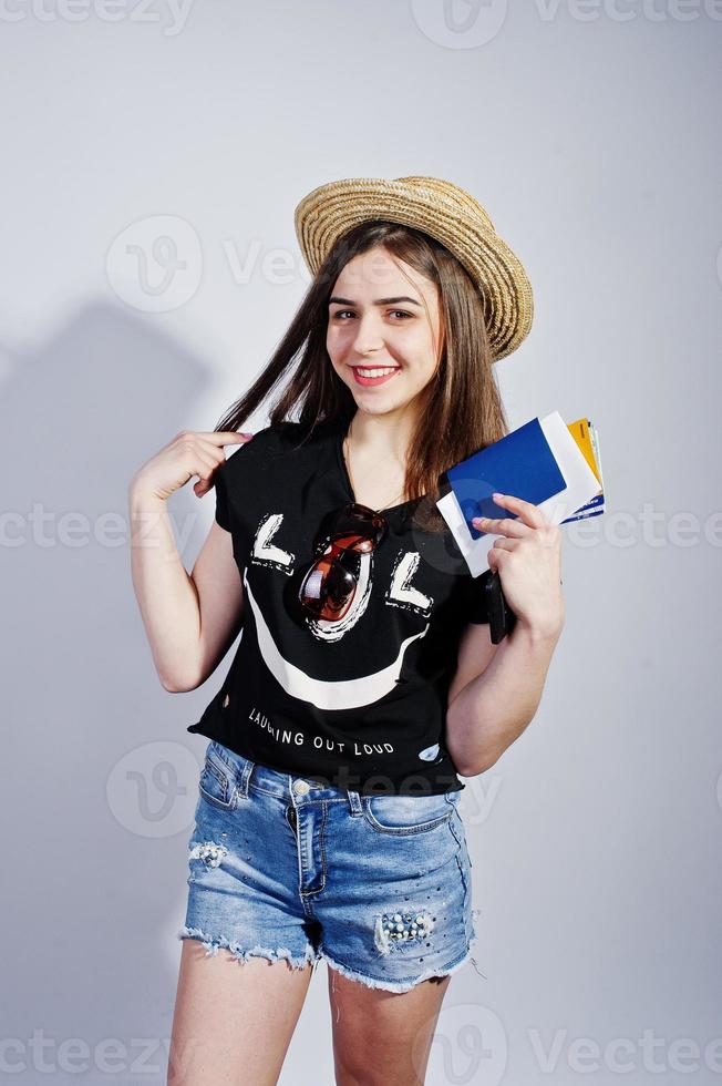 chica turista con pasaporte, vestida con camisa jajaja, pantalones cortos y sombrero aislado en blanco. foto