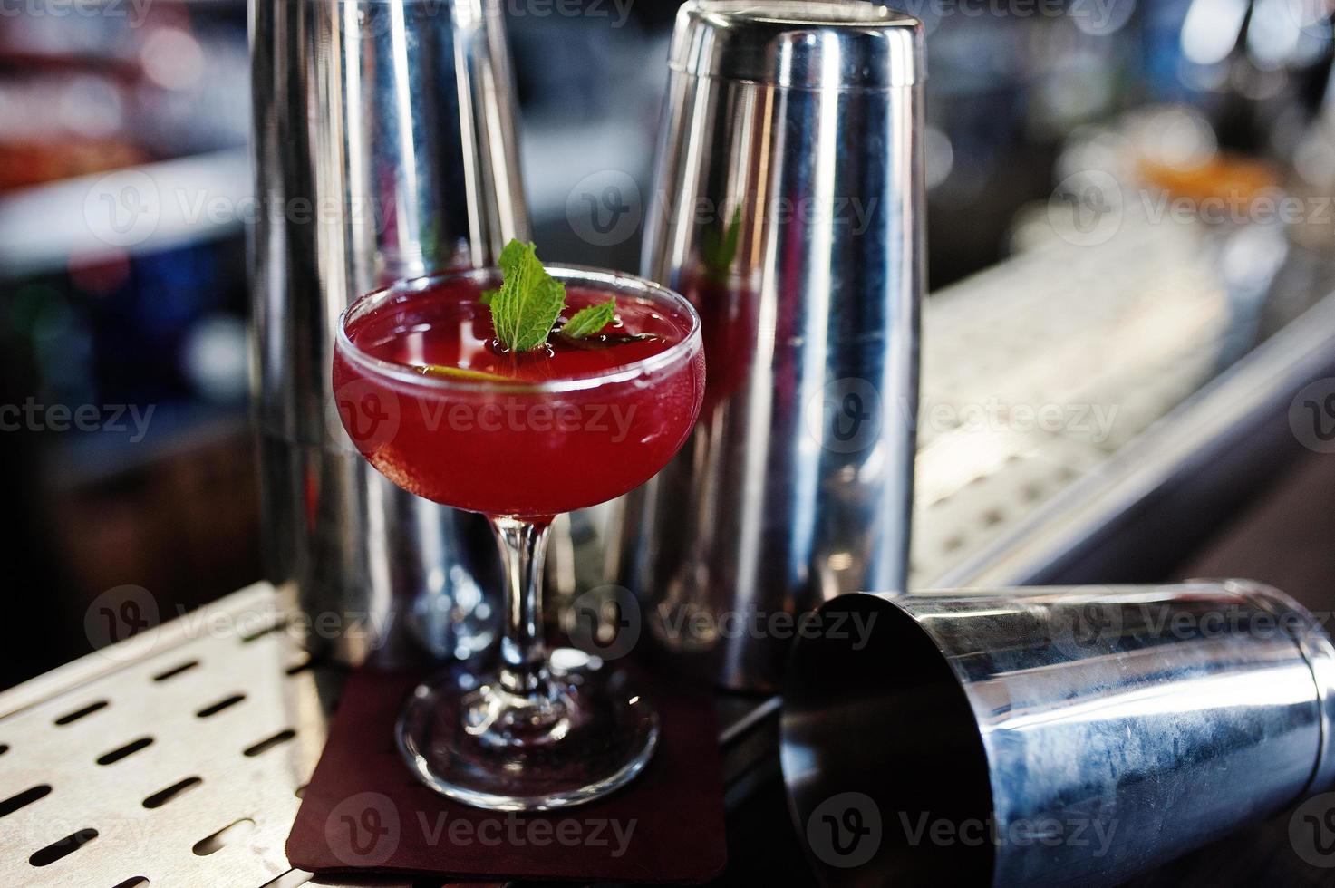 Alcoholic red cocktail with mint on bar table and shakers. photo