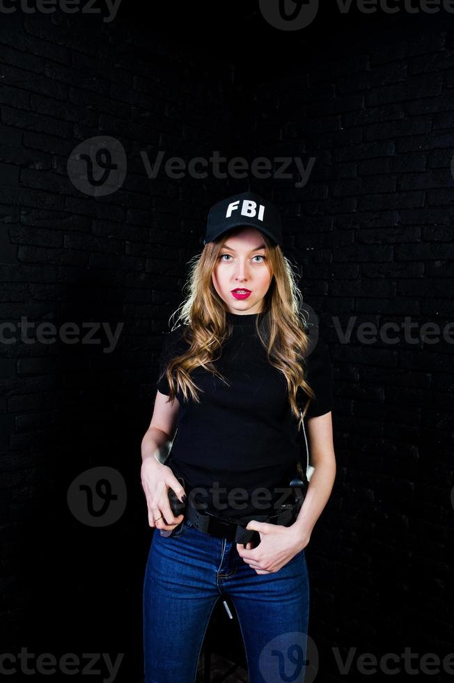 FBI female agent in cap and with gun at studio against dark brick wall. photo