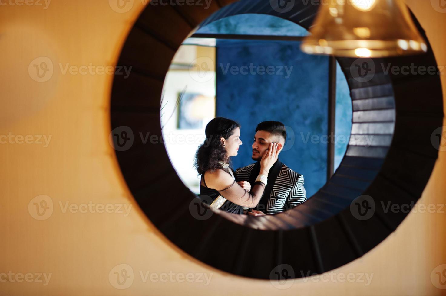 Lovely indian couple in love, wear at saree and elegant suit, posed on restaurant at round circle at wall. photo