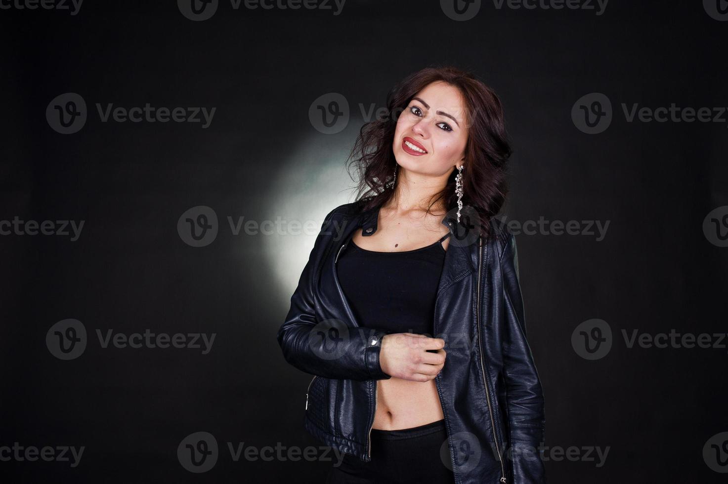 Studio portrait of sexy brunette girl in black leather jacket against black background. photo