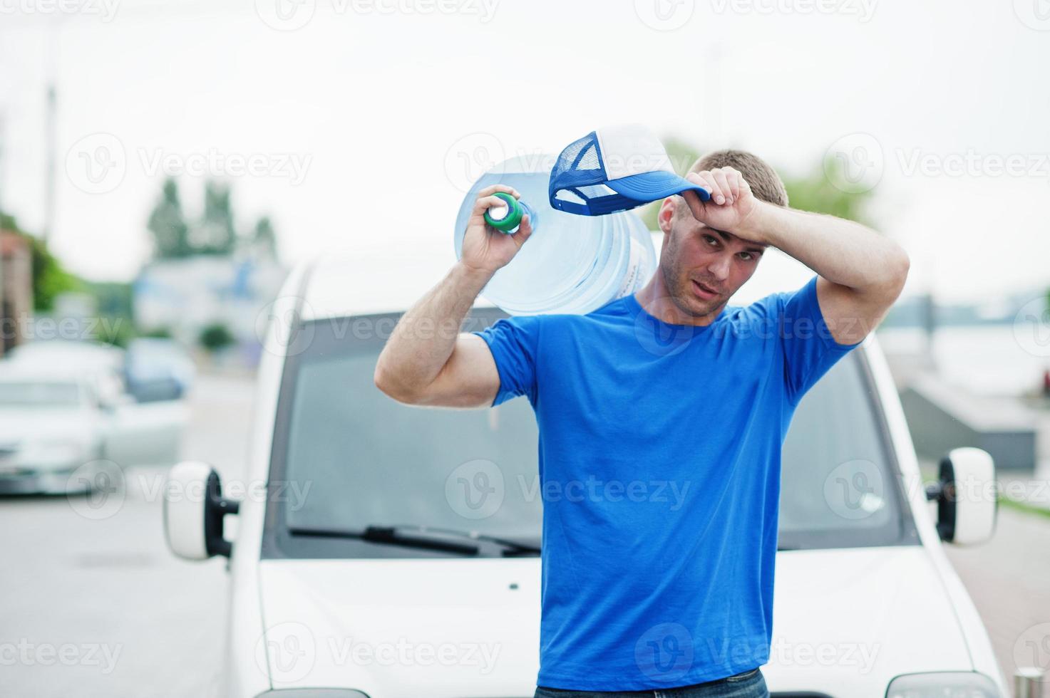 Tyred hard work delivery man in front cargo van delivering bottles of water. photo
