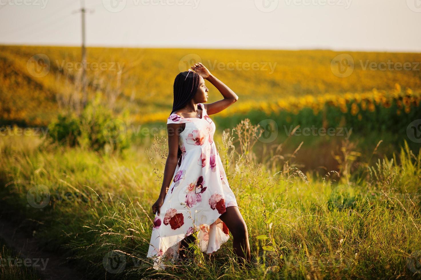 una mujer negra muy joven usa una pose de vestido de verano en un campo de girasoles. foto