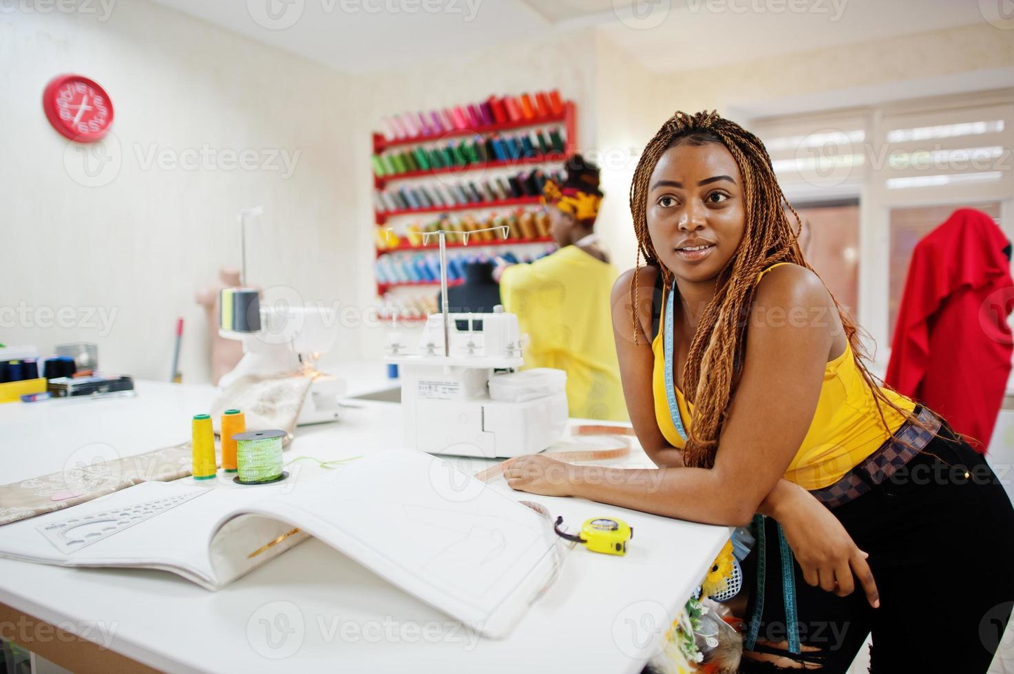 Two african dressmaker woman sews clothes on sewing machine at tailor office. Black seamstress girls. photo