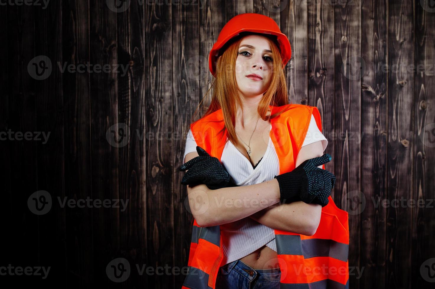 Engineer woman in orange protect helmet and building jacket against wooden background. photo