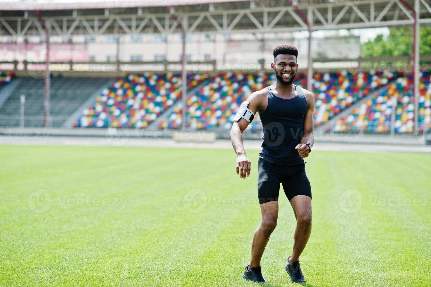 African american male athlete in sportswear doing jump exercise at stadium. photo