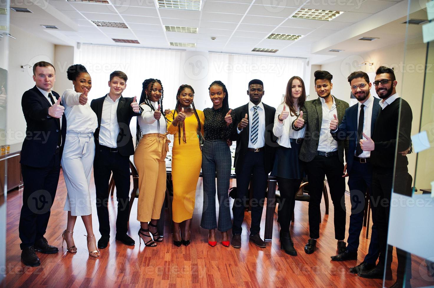 un gran grupo de once empresarios multirraciales parados en la oficina y mostrando el pulgar hacia arriba juntos. grupo diverso de empleados en ropa formal. foto