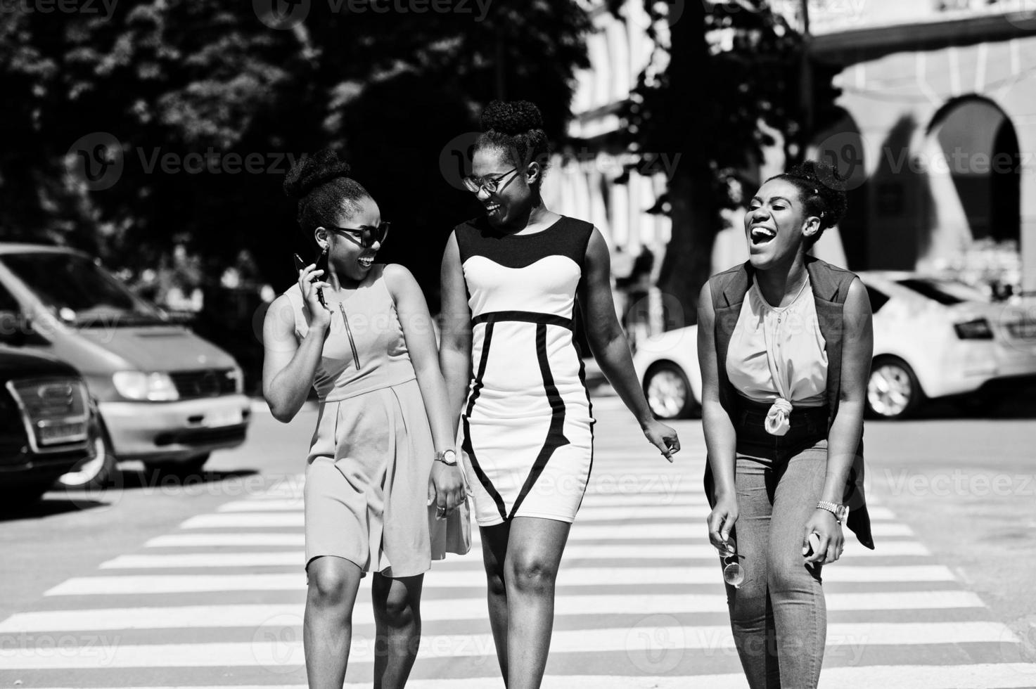 Three stylish african american womans walking on crosswalk or pedestrian crossing, speaking each other and having fun. photo