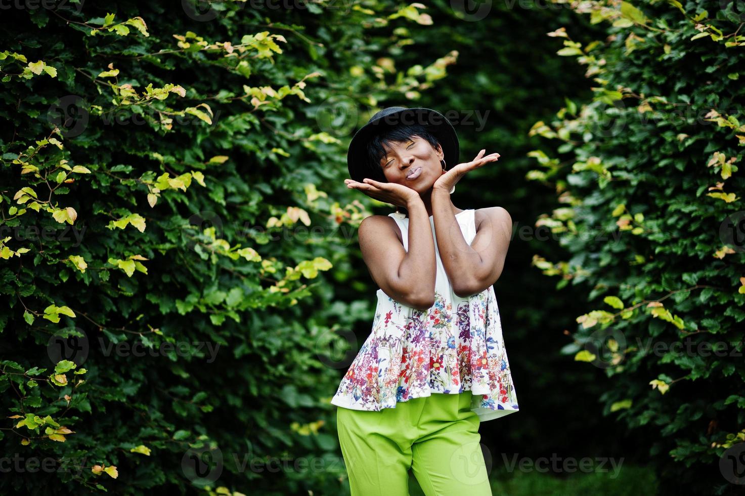 Amazing african american model woman in green pants and black hat posed at park. photo