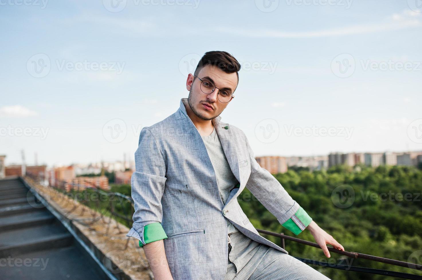 Dreamer stylish macho man in gray suit and glasses posed on the roof. photo
