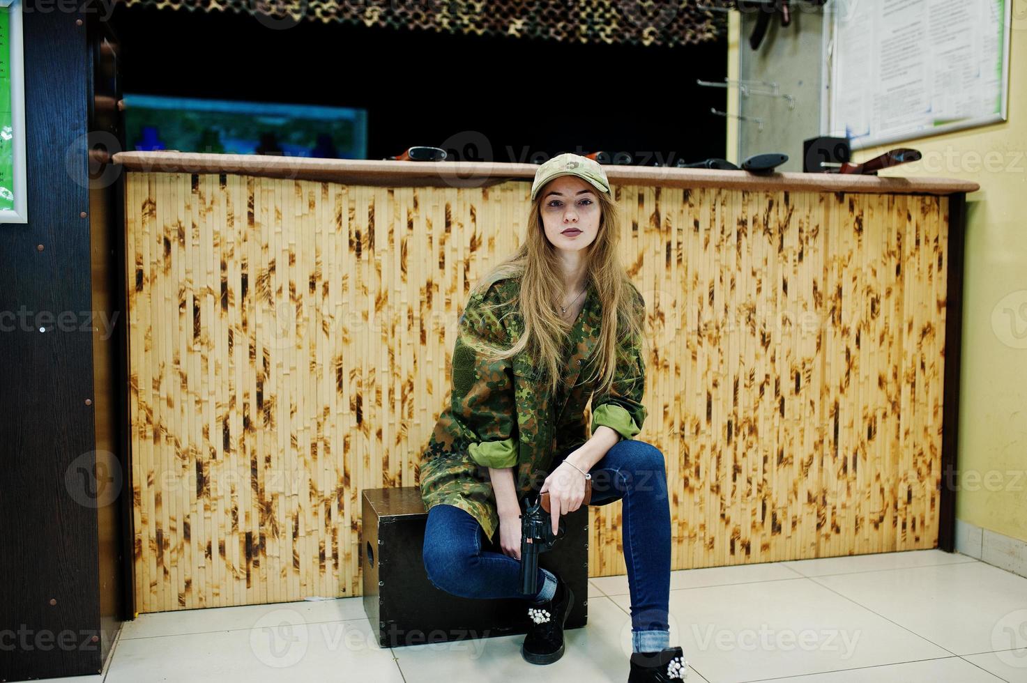 Military girl in camouflage uniform with revolver gun at hand against army background on shooting range. photo