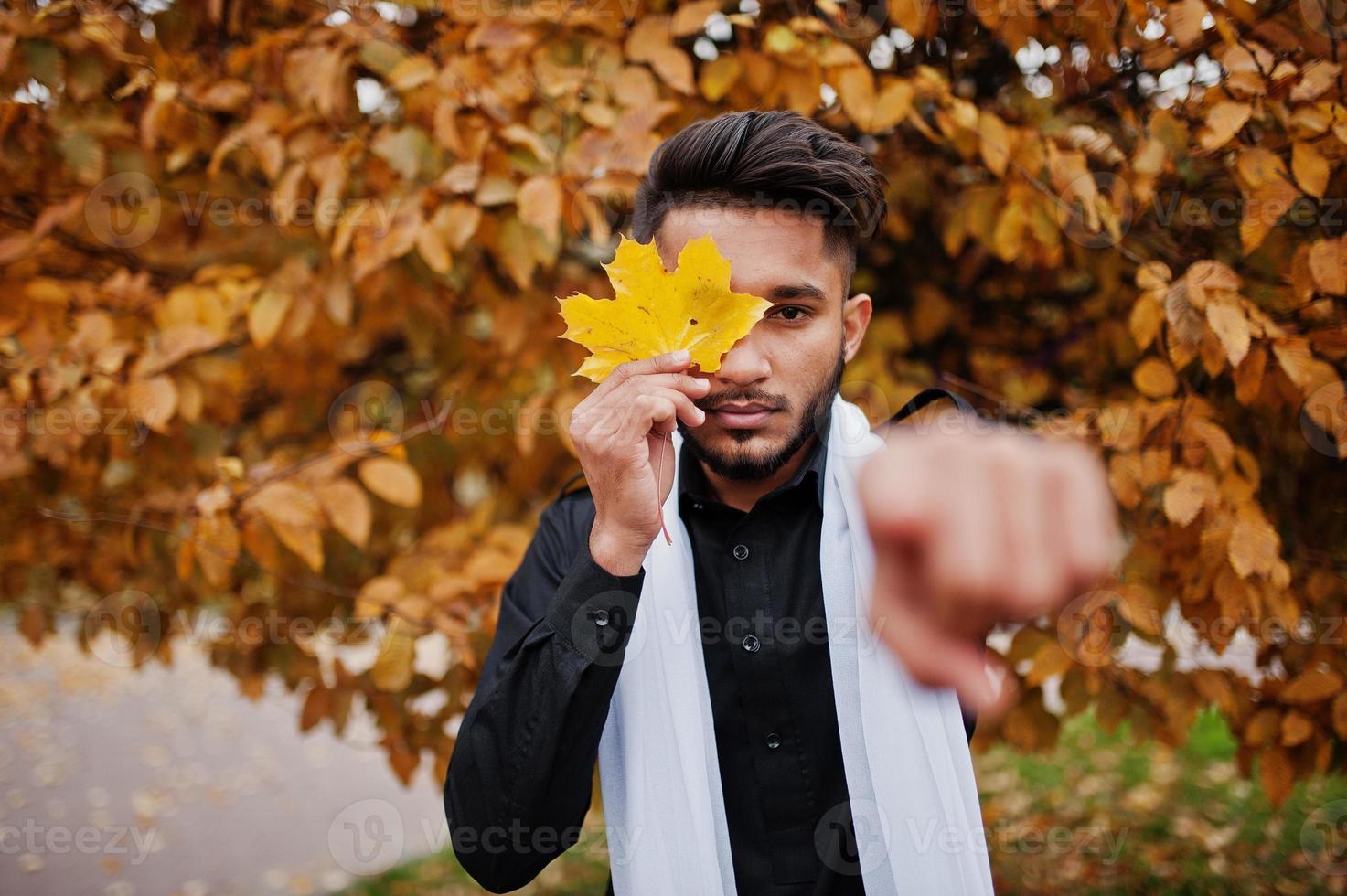 Indian stylish man in black traditional clothes with white scarf posed outdoor against yellow autumn and show finger. photo