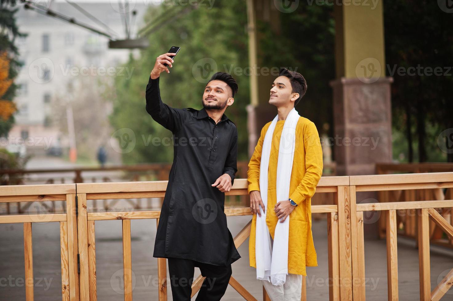Two indian stylish mans friends in traditional clothes posed outdoor and making selfie on phone. photo