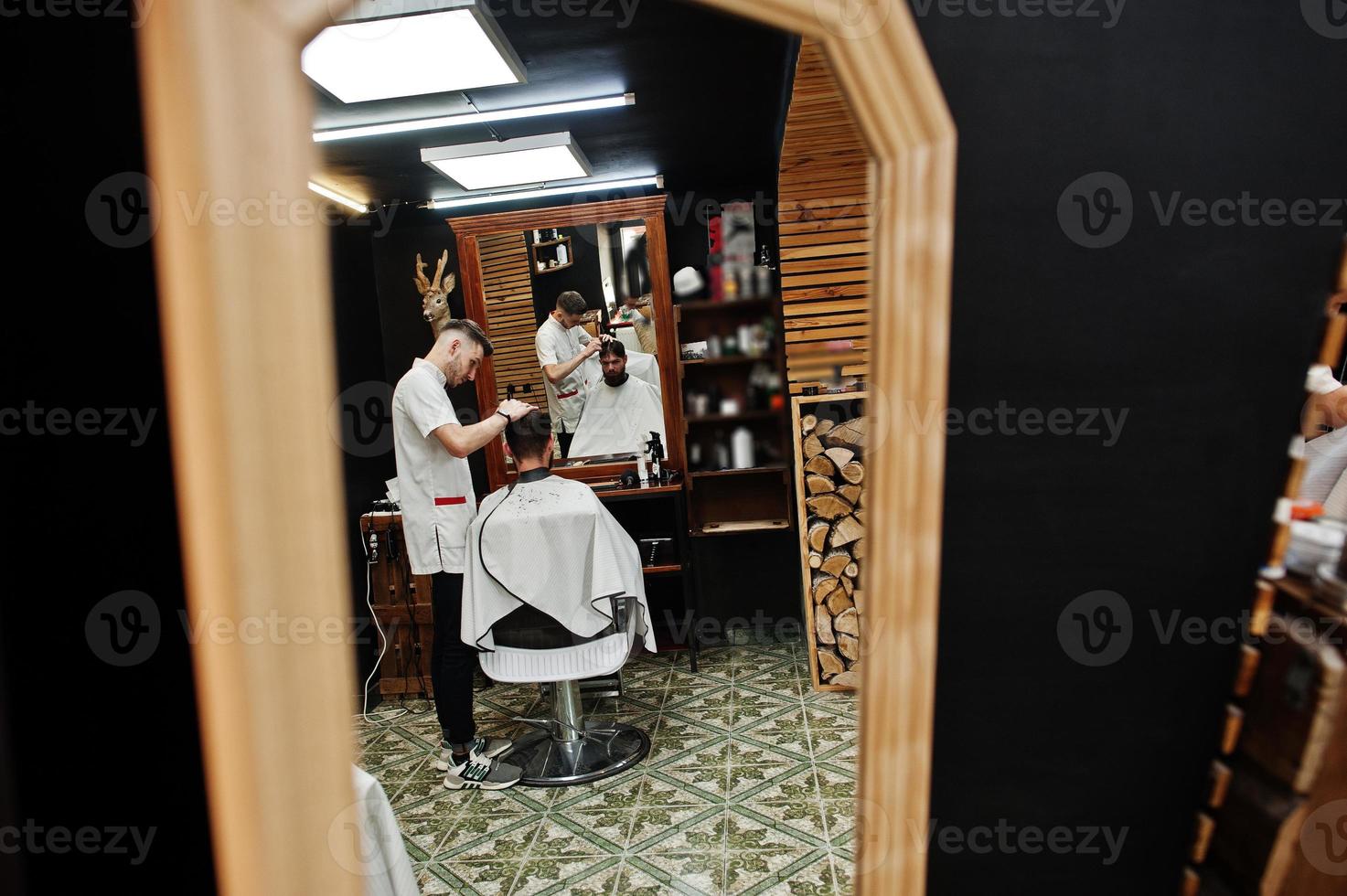 Young bearded man getting haircut by hairdresser while sitting in chair at barbershop. Barber soul. photo