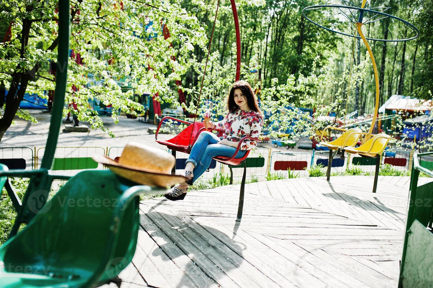 Portrait of brunette girl in pink glasses and hat with ice cream at amusement park. photo