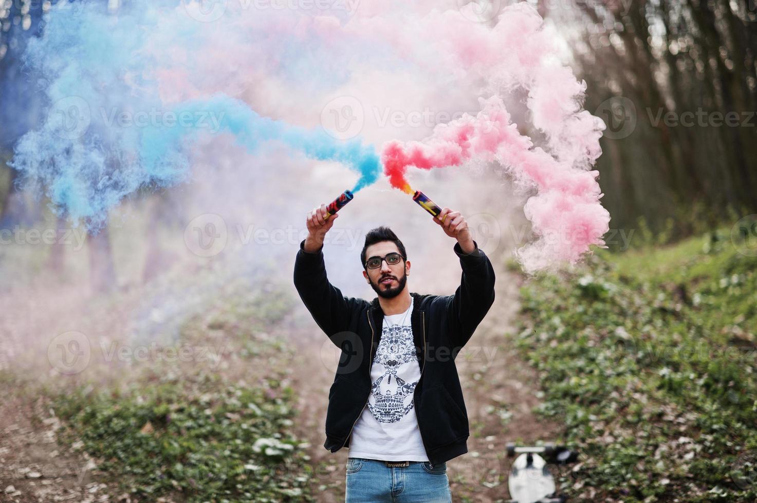Street style arab man in eyeglasses hold hand flare with red and blue smoke grenade bomb. photo